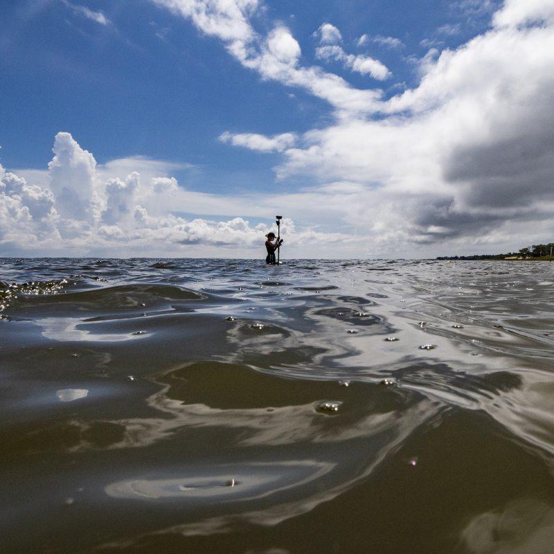 A figure in the ocean holding a piece of scientific equipment above the waves