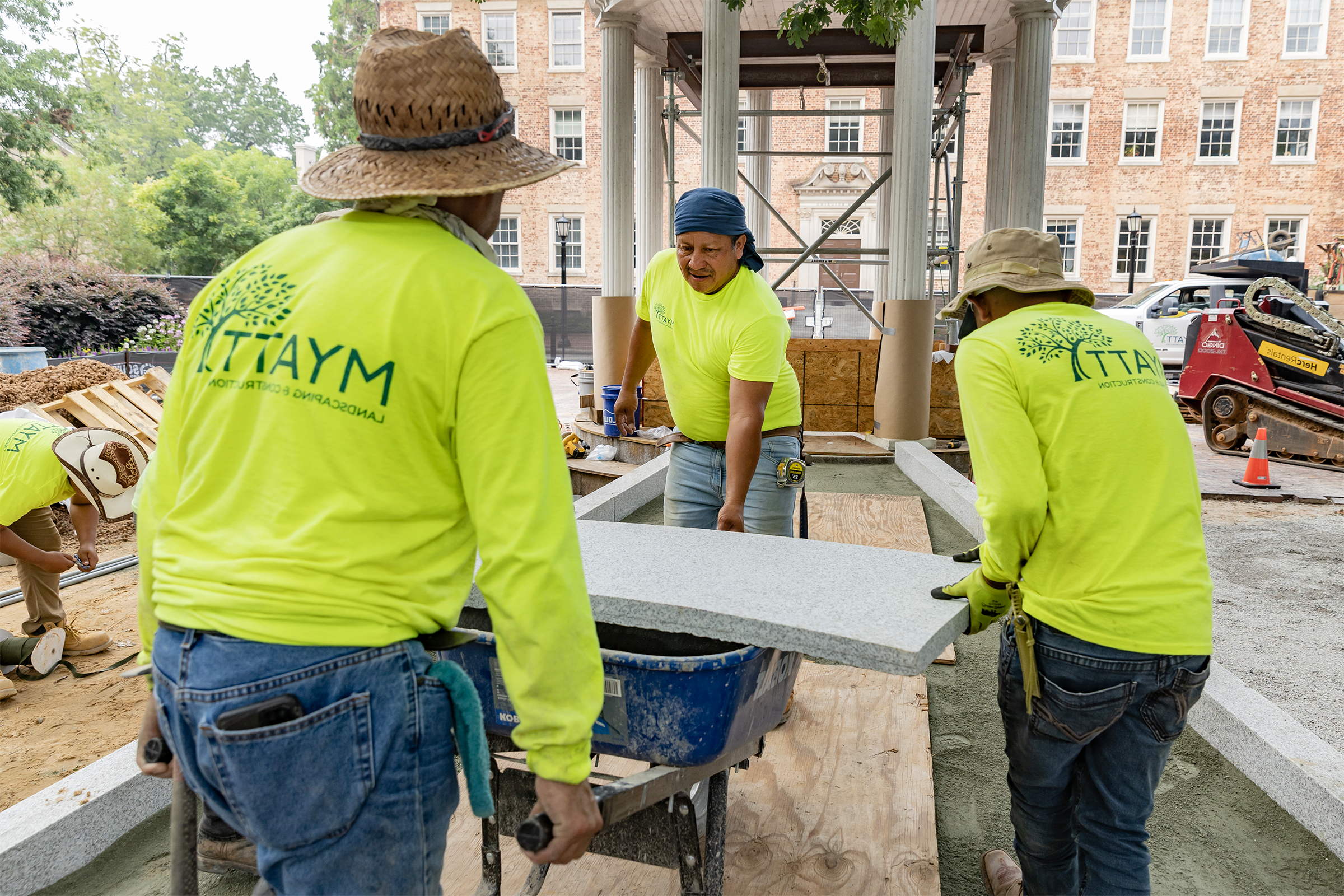 Three workers using a wheelbarrow to transport granite slab.