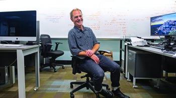 Daniel Anderson sitting at computer in front of whiteboard.