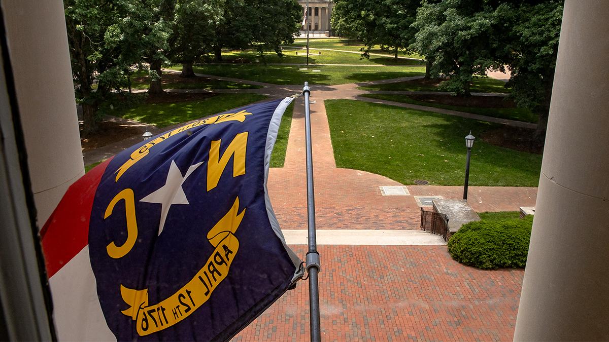 Photograph of the North Carolina flag hanging from South Building.